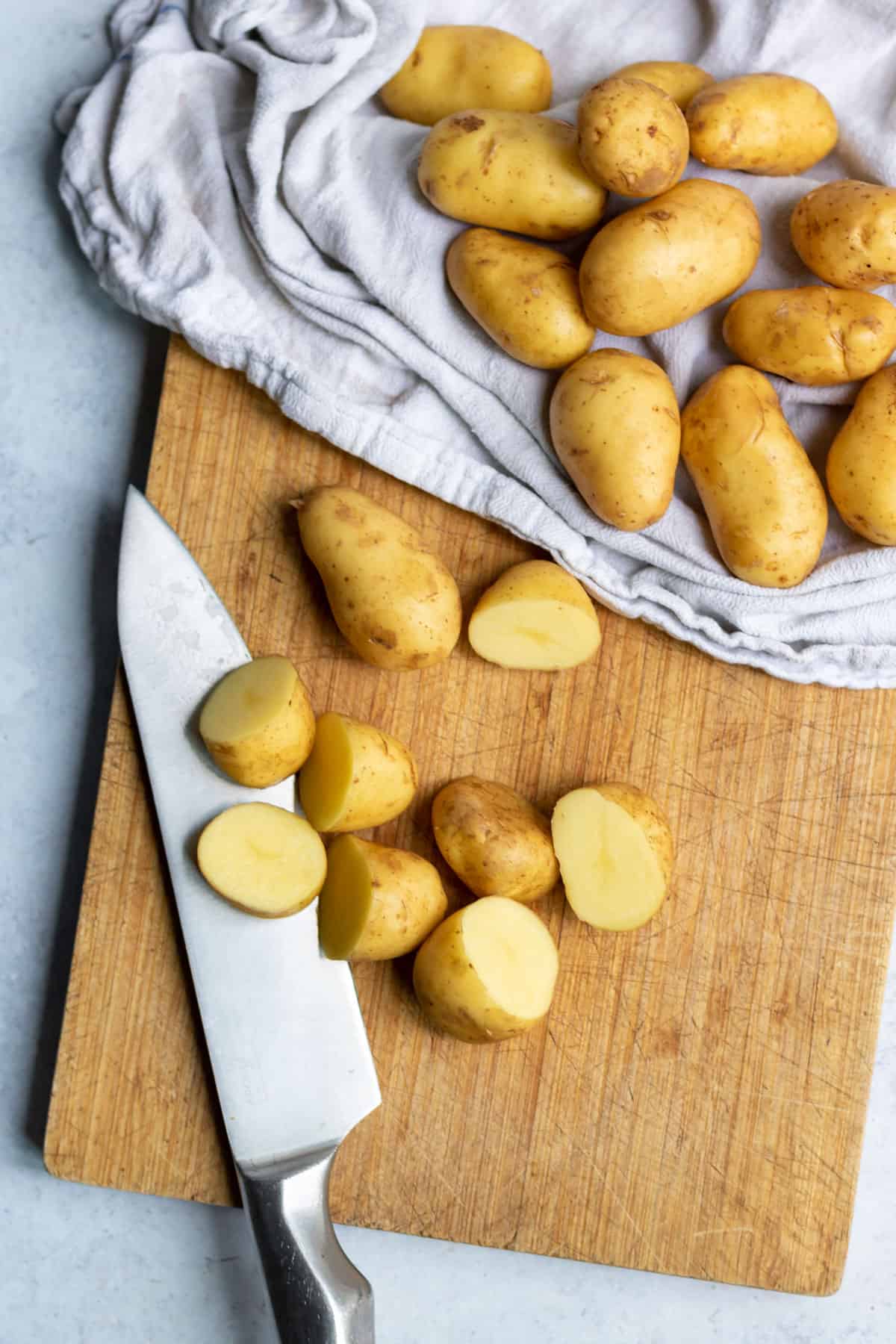 Cutting baby potatoes in half on a cutting board.