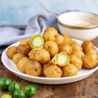 A table with a dish of beer battered deep fried brussels sprouts and a bowl of dip.