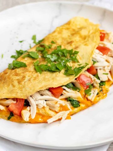 A folded chicken omelette on a plate topped with chopped herbs.