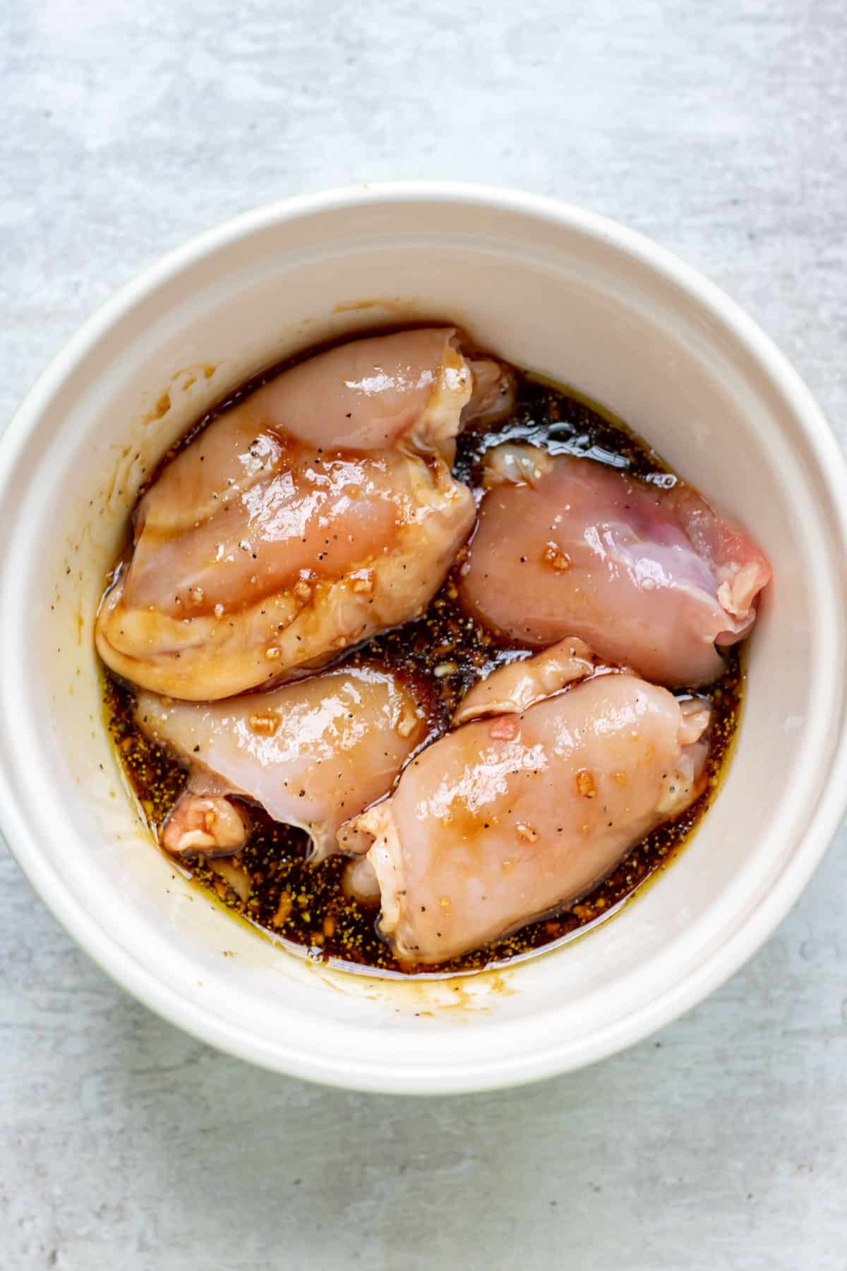 Bowl of skinless boneless chicken thighs in marinade.