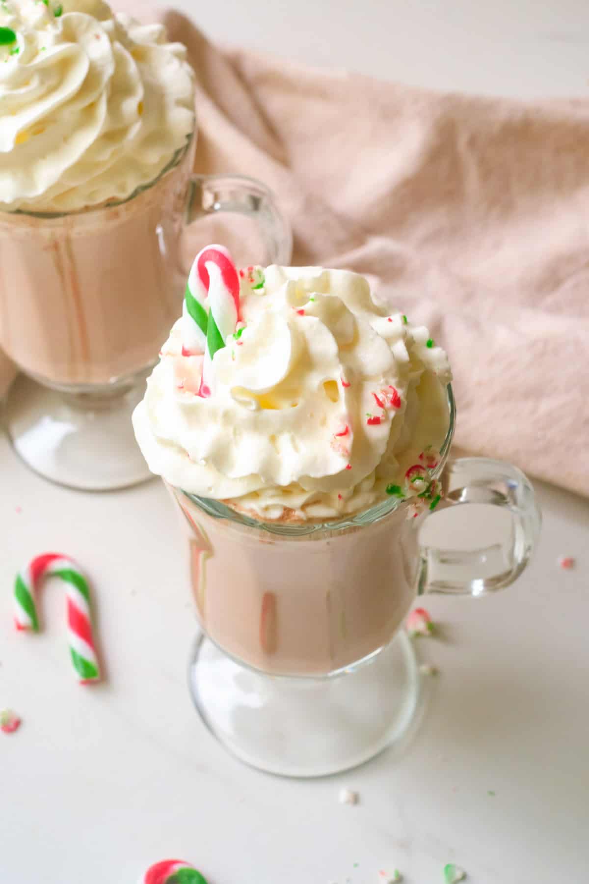 Candy cane sticking out of whipped cream on top of hot chocolate.