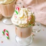 Candy cane sticking out of whipped cream on top of hot chocolate.