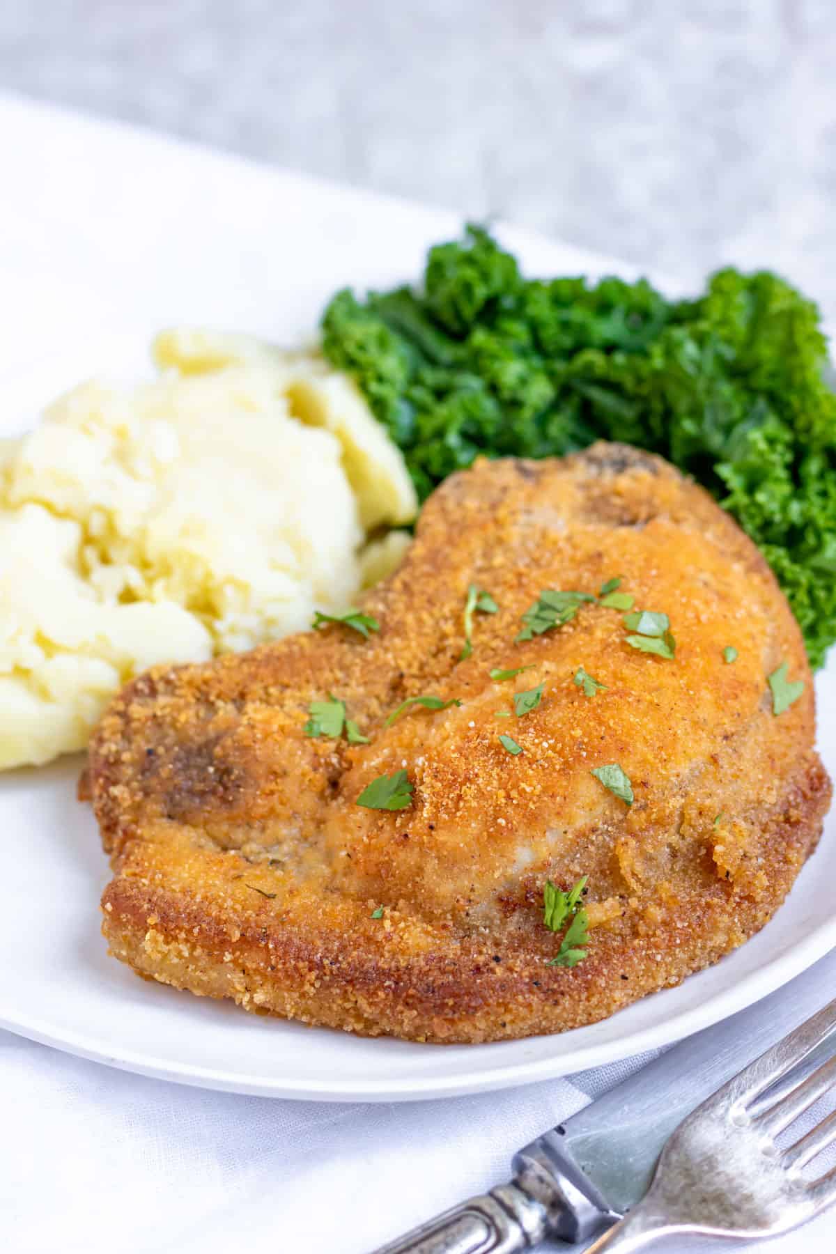 Plate with a breaded pork chop, mashed potato and greens.