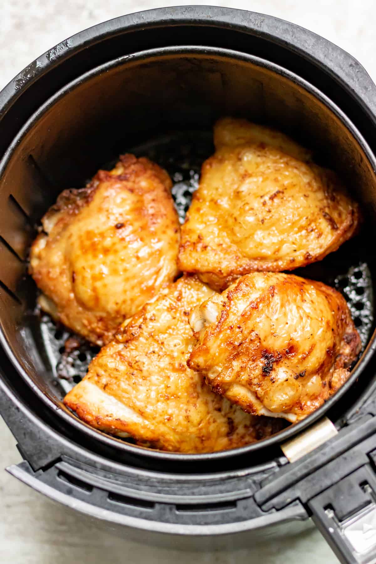 Chicken thighs in an air fryer basket.