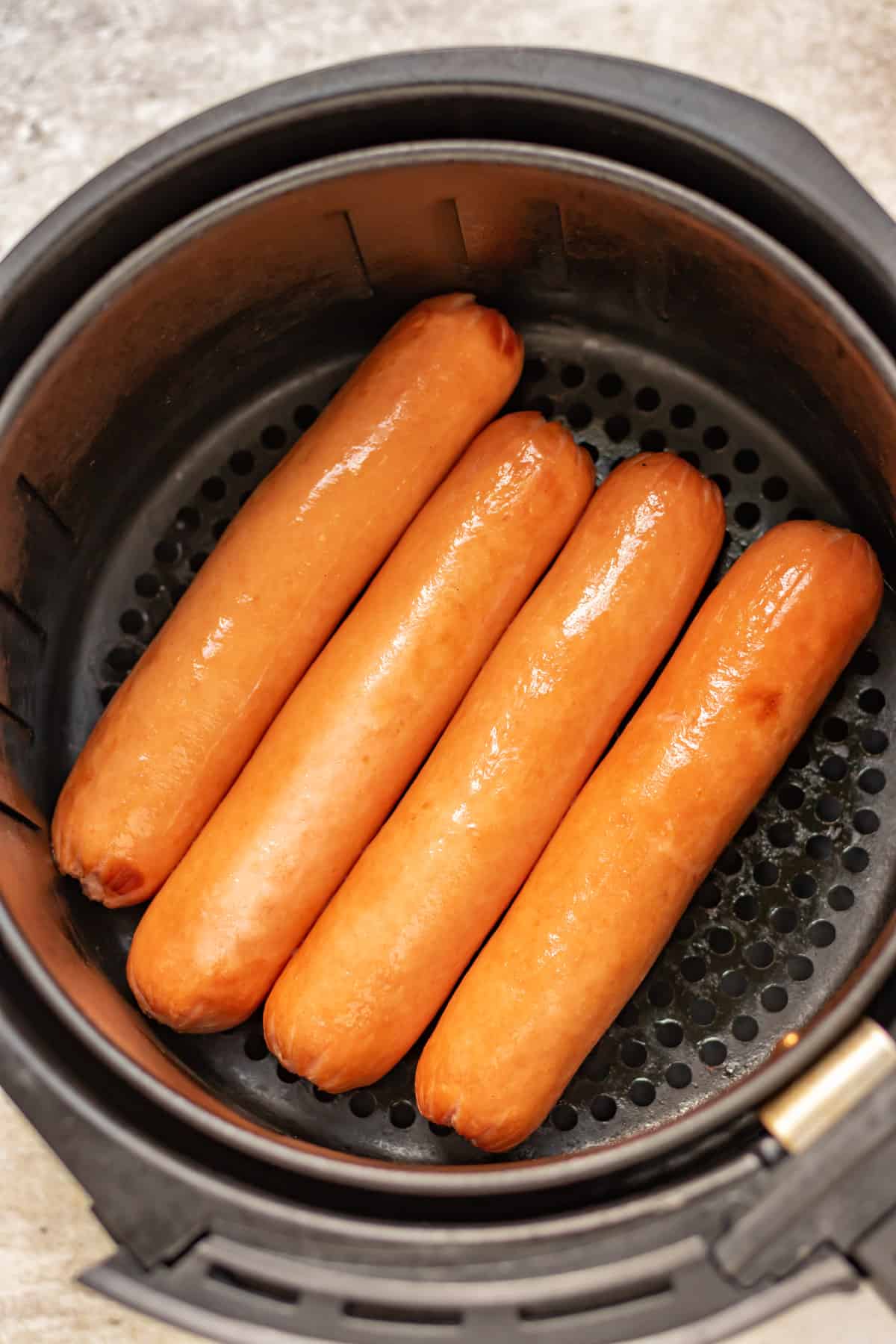 Cooked hot dogs in air fryer basket.