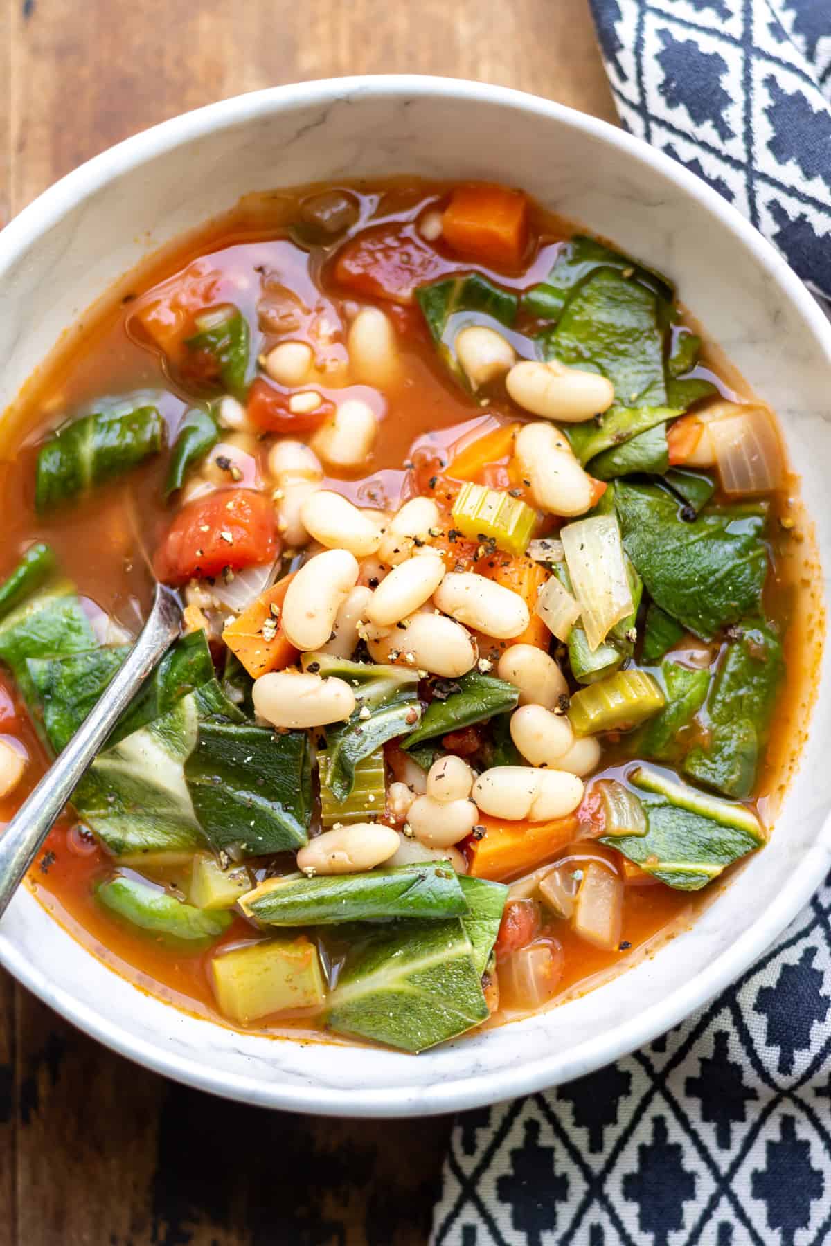 Close up of a bowl of soup with silverbeet chard, beans, vegetables and tomatoes.