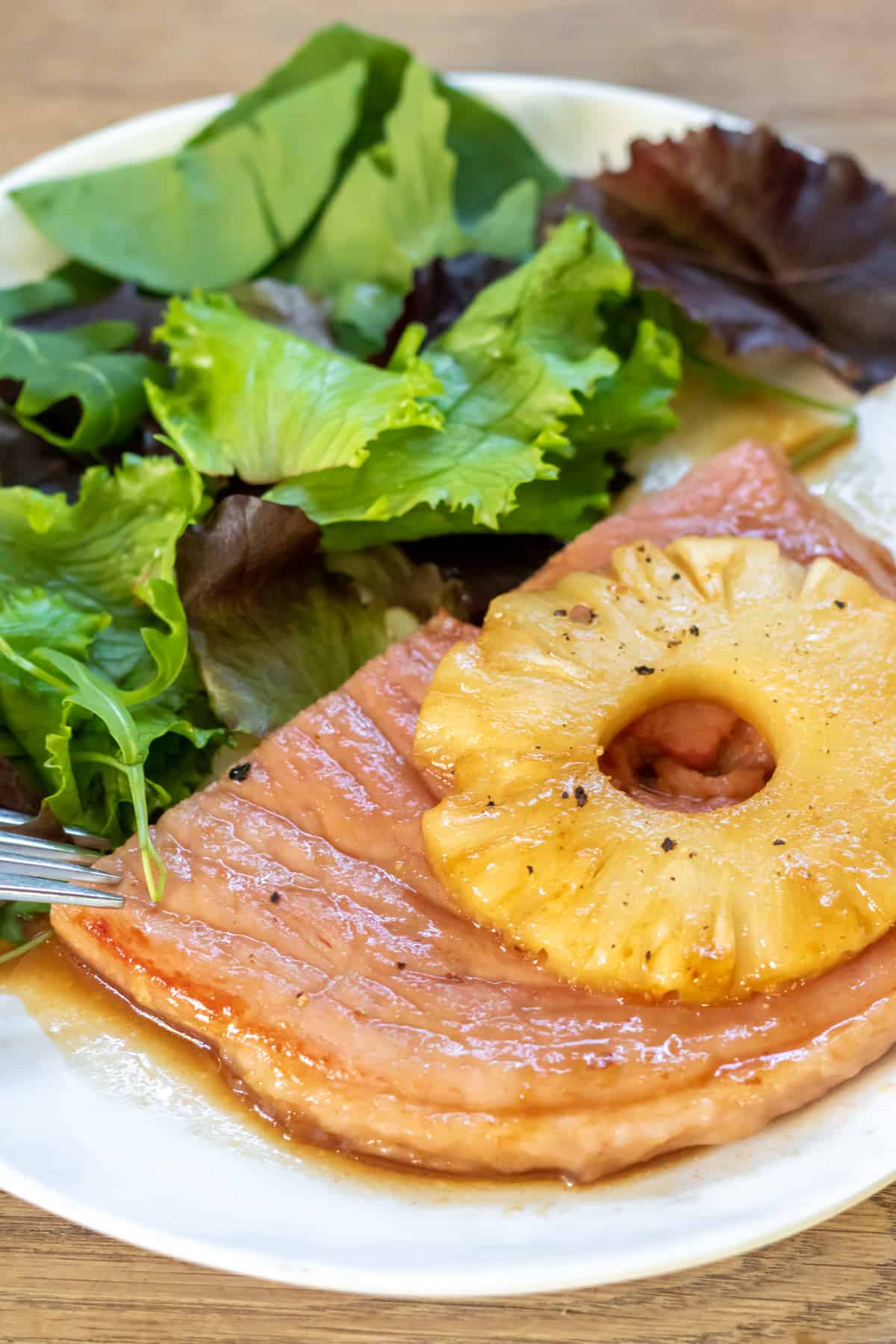 A plate with a glazed ham steak, pineapple and salad.