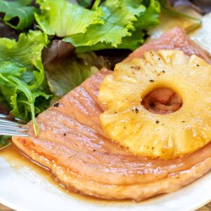 Close up of a fried ham steak on a plate topped with a pineapple ring.