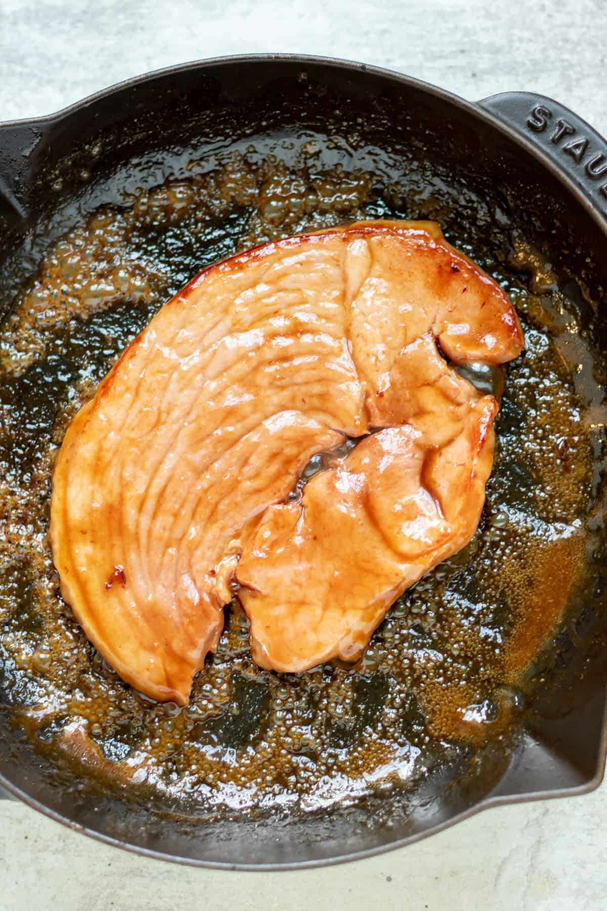 Flipped ham steak in a pan of glaze.