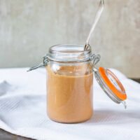 A jar of sauce with a spoon, on a table.