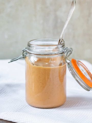 A jar of sauce with a spoon, on a table.