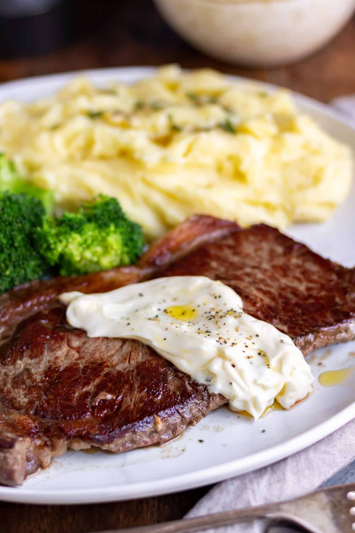 A plate with mashed potato, broccoli and steak with a dollop of truffle aioli.