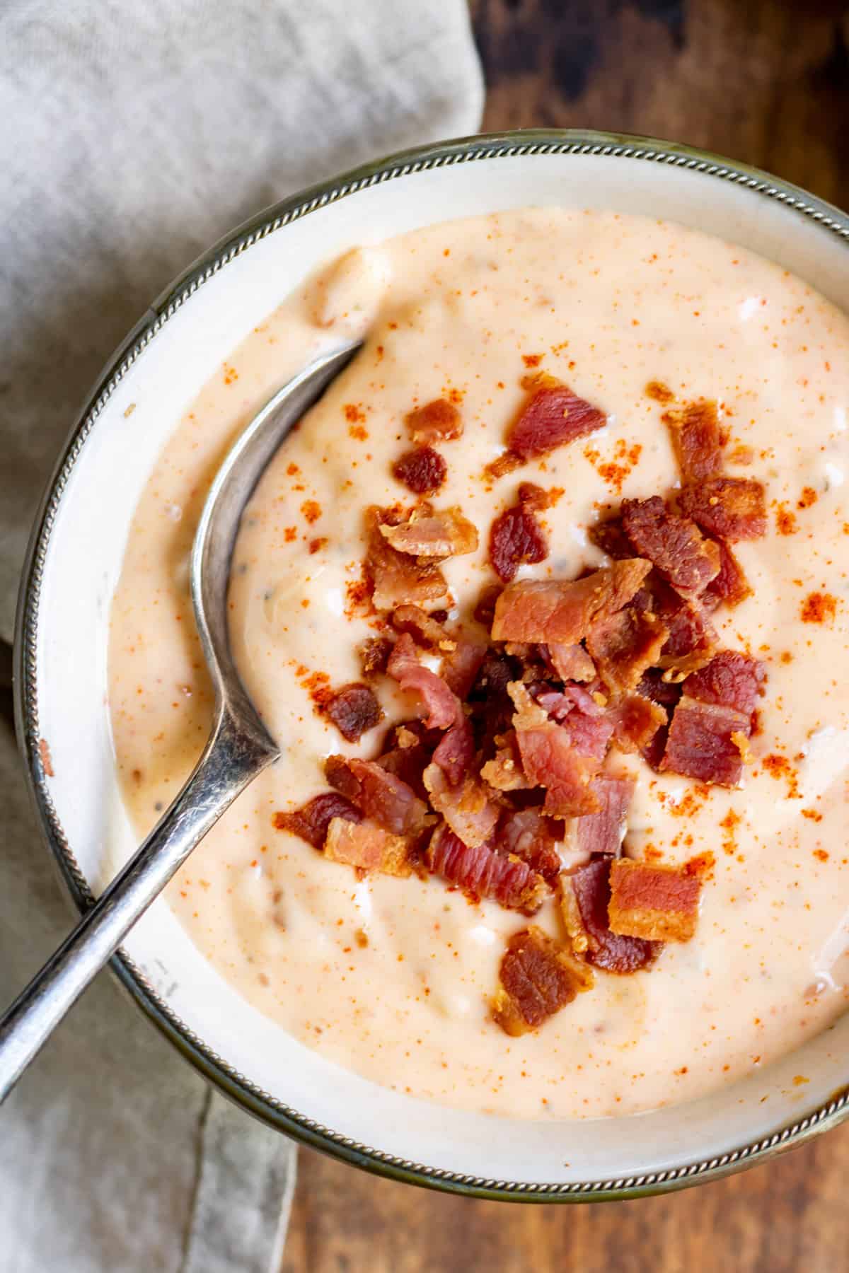 Spoon in a bowl of bacon aioli with extra bacon on top.