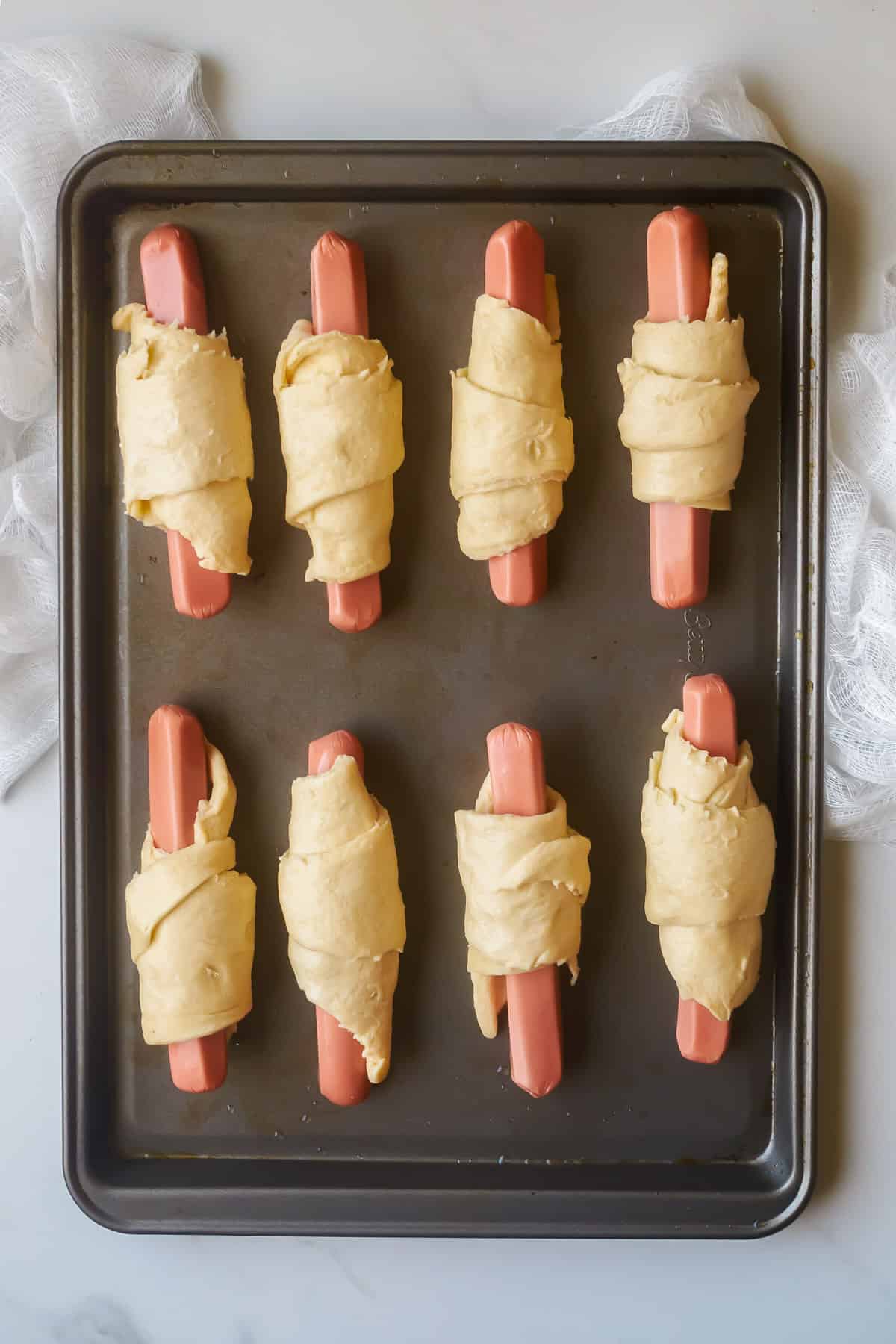 Hot dogs wrapped in crescent dough on a baking sheet ready to cook.