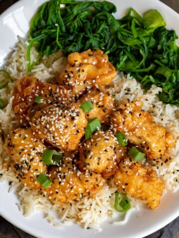 Plate of honey sesame chicken, rice and spinach on a table.