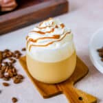 Wooden board, glass of caramel frappuccino, topped with whipped cream and caramel sauce.