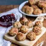 A wooden board with cranberry turkey meatballs on toothpicks.