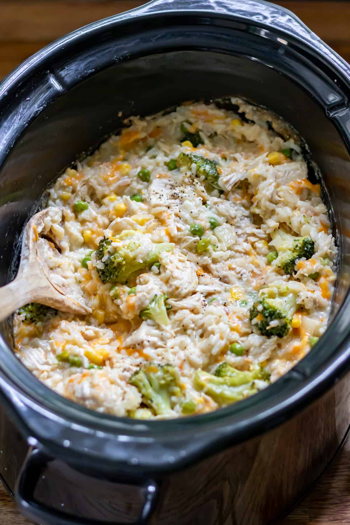 Wooden spoon in a slow cooker of cheesy chicken and rice.