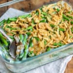 Glass dish of green bean casserole on a wooden table.
