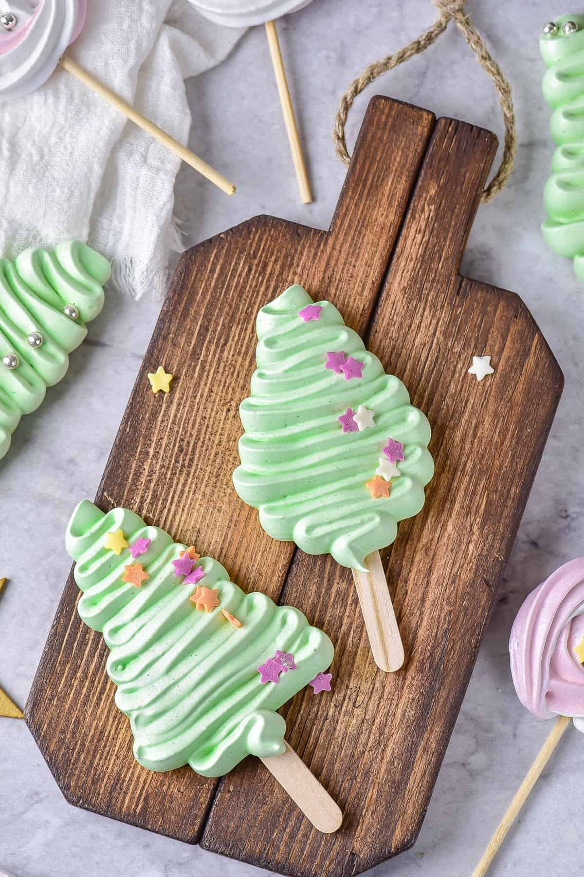 Two meringues shaped like Christmas trees on a wooden board.