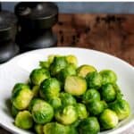 Wooden table with a dish of sprouts, and text: Easy Microwave Brussels Sprouts.