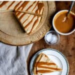 A table with pie and slices on plates, with text: No bake Salted Caramel Cheesecake Pie.
