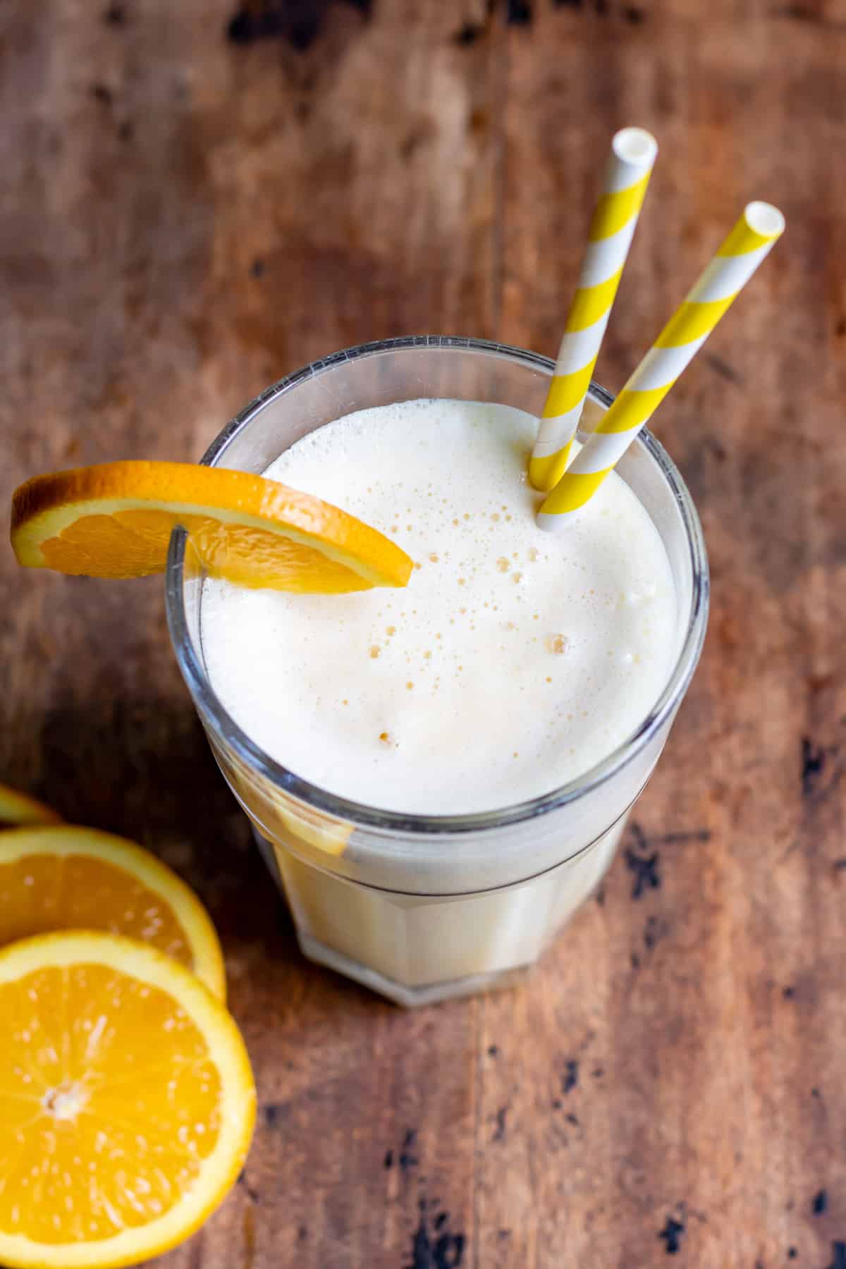 Wooden table with a glass of orange julius, with a straw and slices of orange.