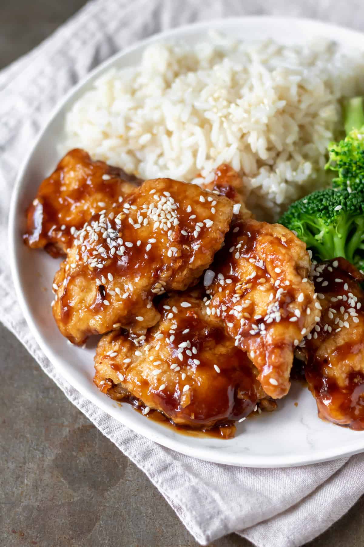 Close up of sweet chili chicken on a plate, with rice and broccoli.