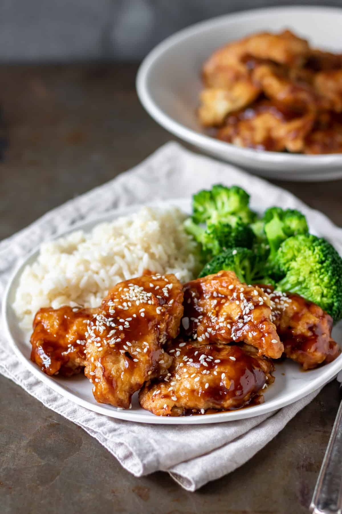 Table with a plate of rice, broccoli and sweet chili chicken.
