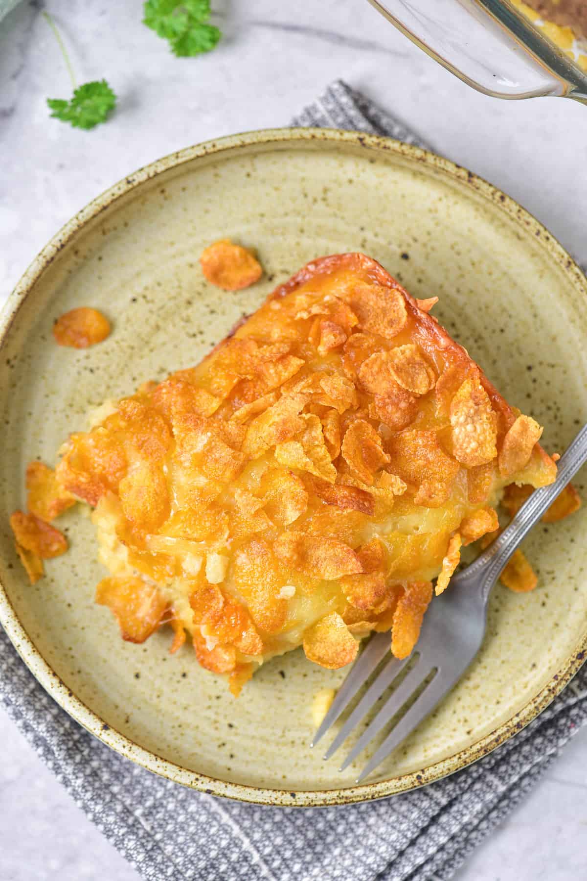 Looking down at a plate of hashbrown casserole topped with cornflakes and cheese.
