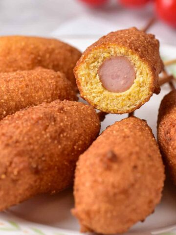 A plate of corn dogs with one cut open to show the hot dog inside.