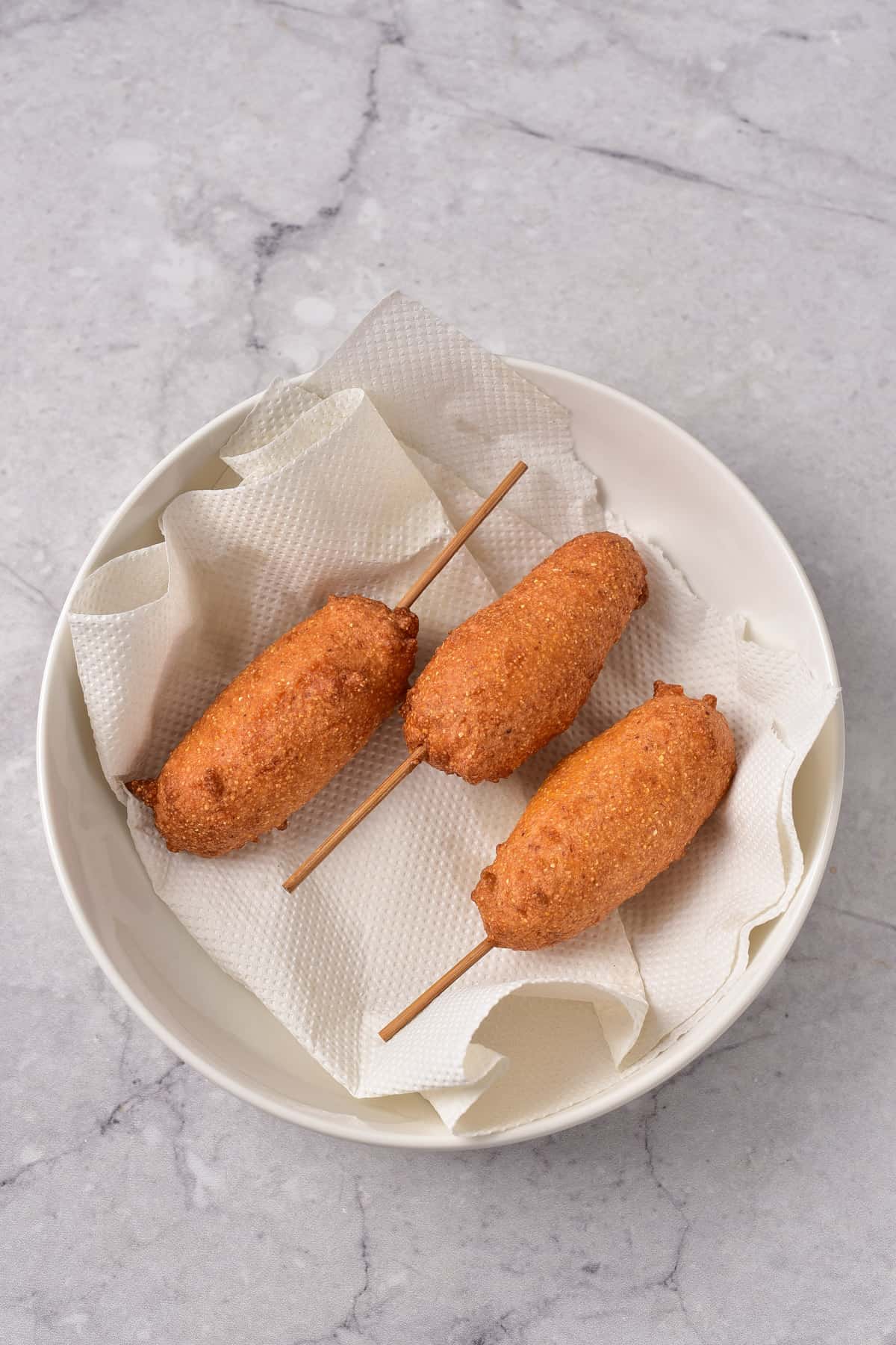 Cooked corn dogs draining on a dish lined with paper towels.