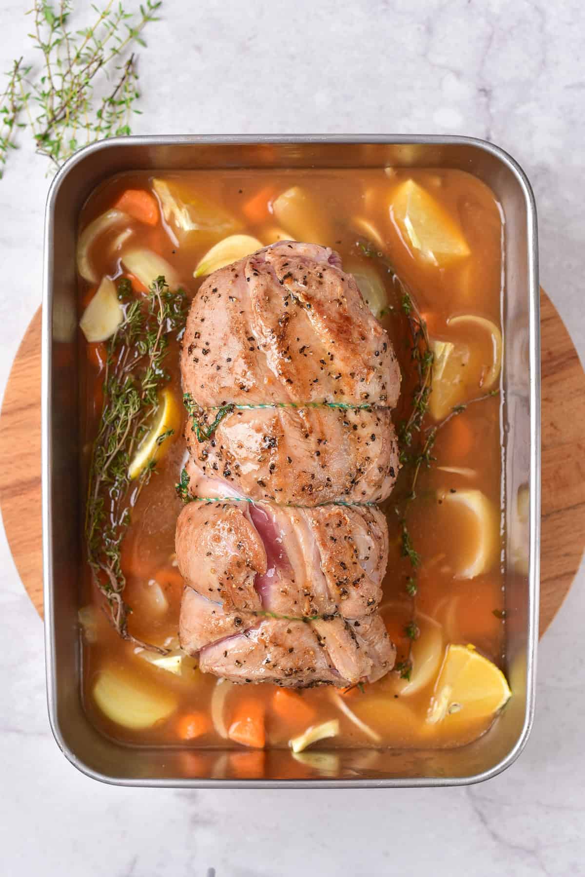 Seared rolled lamb, on a baking tray above vegetables.