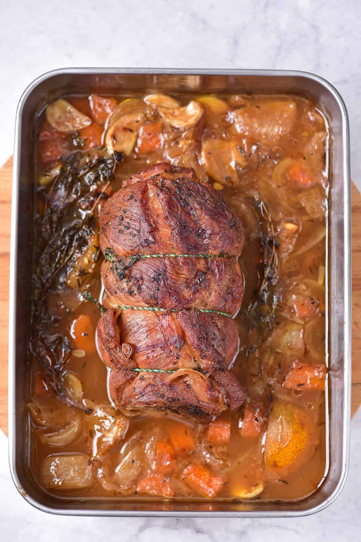 Roasted rolled lamb on a baking tray with vegetables.