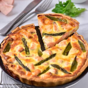 A slice of salmon quiche with asparagus being taken out of the full quiche.