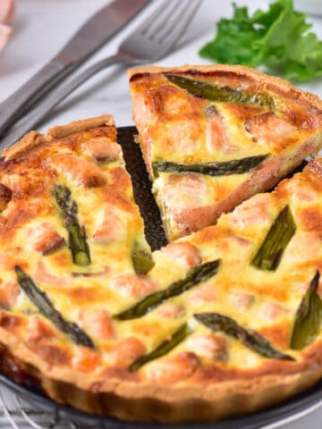 A slice of salmon quiche with asparagus being taken out of the full quiche.