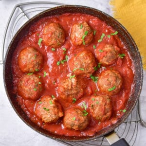 Looking down at a skillet of baked beef meatballs in tomato sauce.