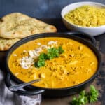 Table with a dish of slow cooker chicken korma, next to rice and naan.