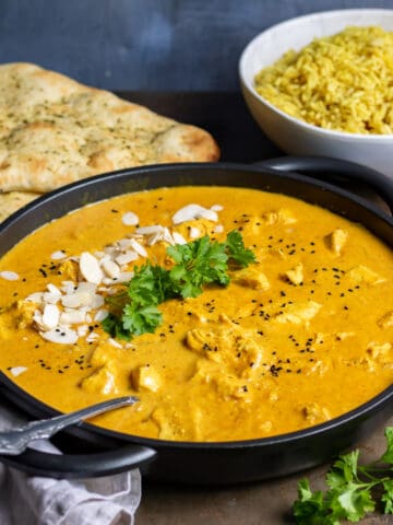 Table with a dish of slow cooker chicken korma, next to rice and naan.