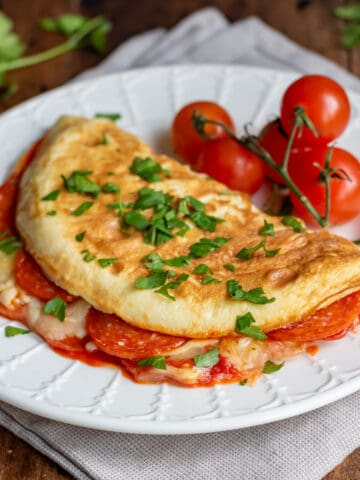 Folded pizza omelet (filled with pepperoni, pizza sauce and mozzarella) on a plate.
