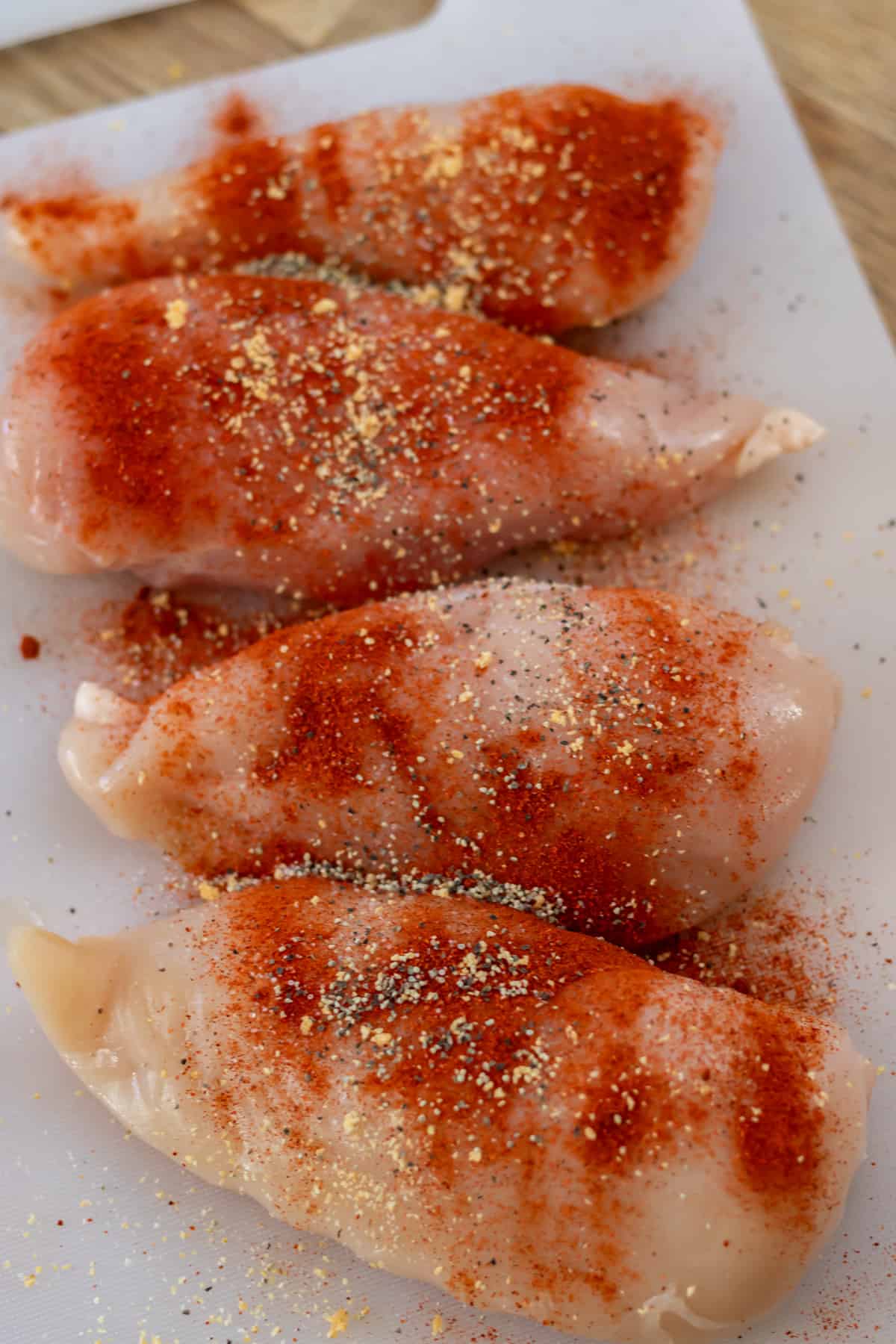 Seasoned raw chicken breasts on a cutting board.