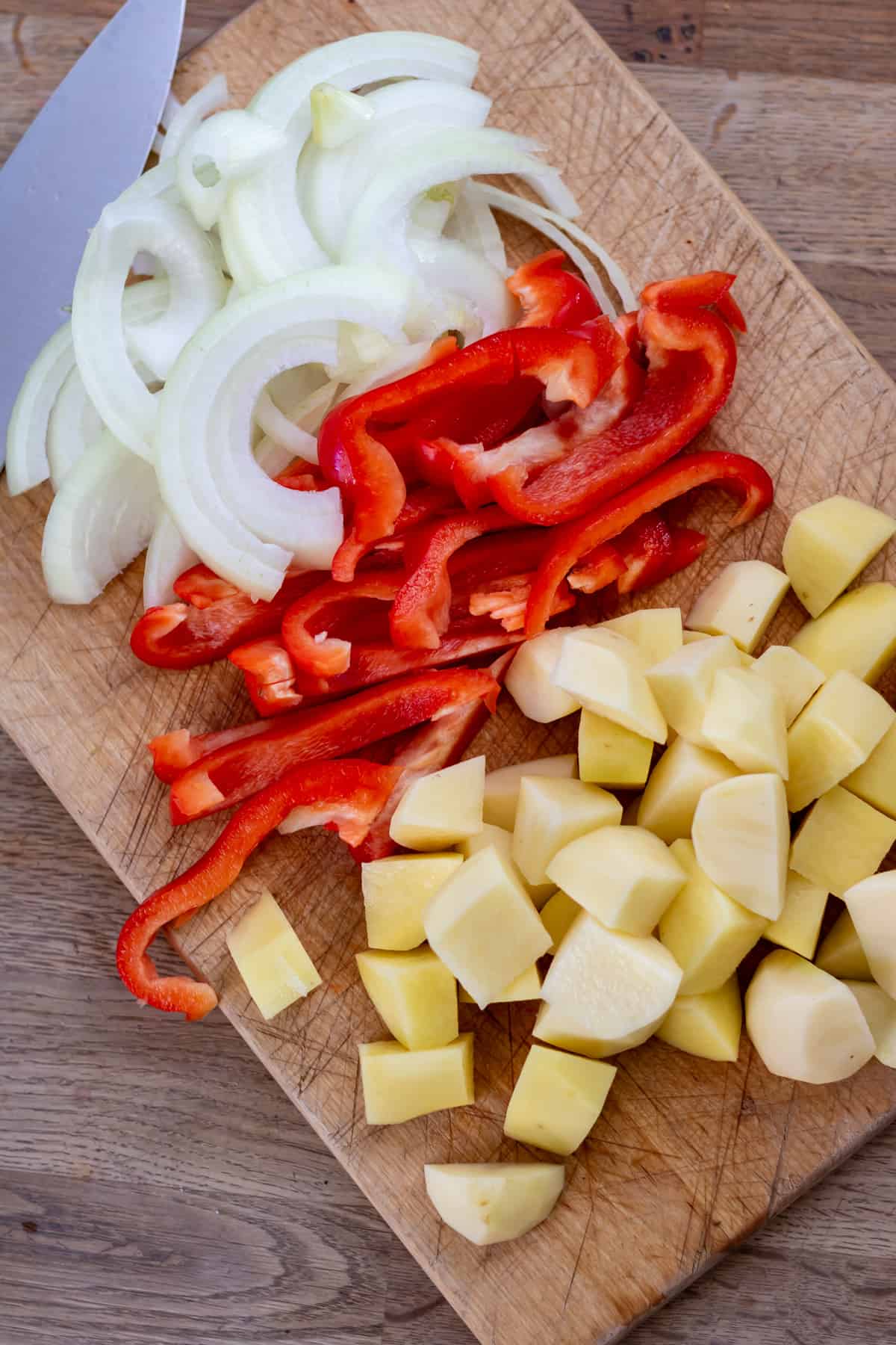Cutting board with sliced onions, peppers and diced potatoes.