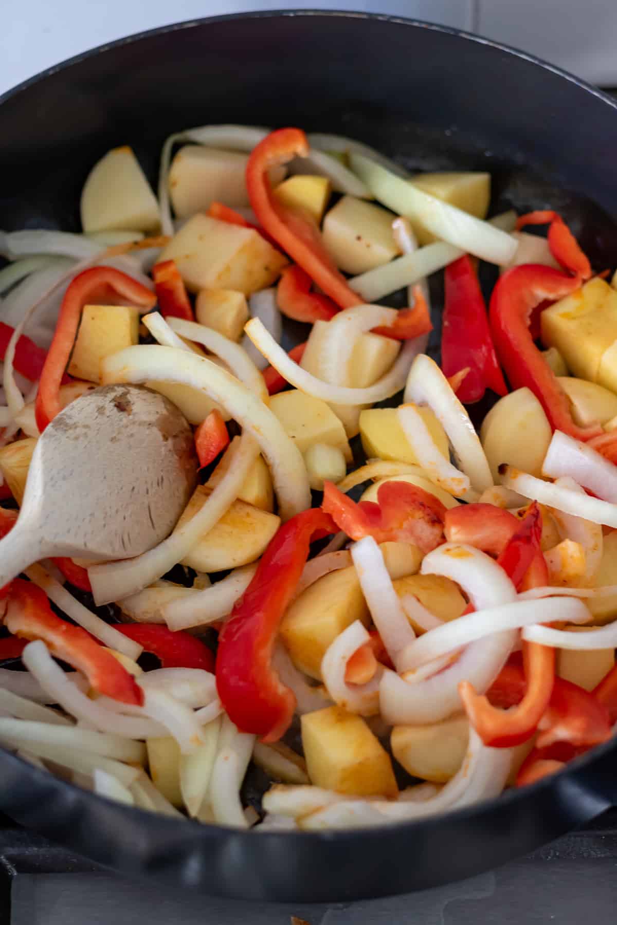 Diced potatoes, sliced onions and peppers in a pan cooking.