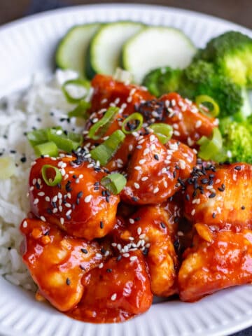 Close up of Korean gochujang chicken on a plate with rice and green vegetables.