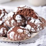 A plate of chocolate crinkle cookies, and one on top has a bite out.