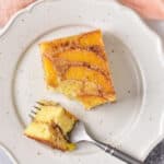 Close up of a plate with a square of peach upside down cake, with a forkful next to it.