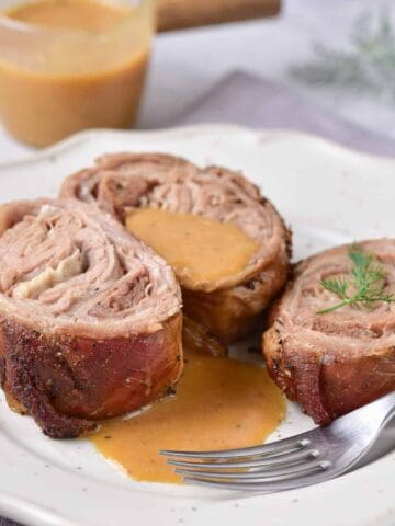 Plate of roasted rolled lamb with gravy and a fork.