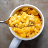 A forkful of microwave macaroni and cheese coming out of a mug.