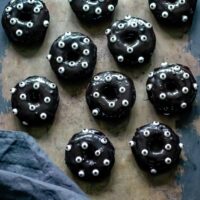 A metal tray with rows of baked black chocolate halloween donuts decorated with candy eyes.