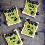 A metal table with four Halloween Frankenstein Toasts - with guacamole and olives.
